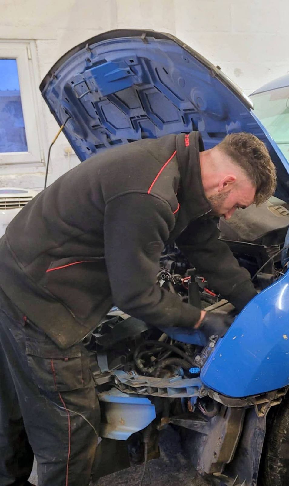 Mechanic working under the bonnet of a blue car