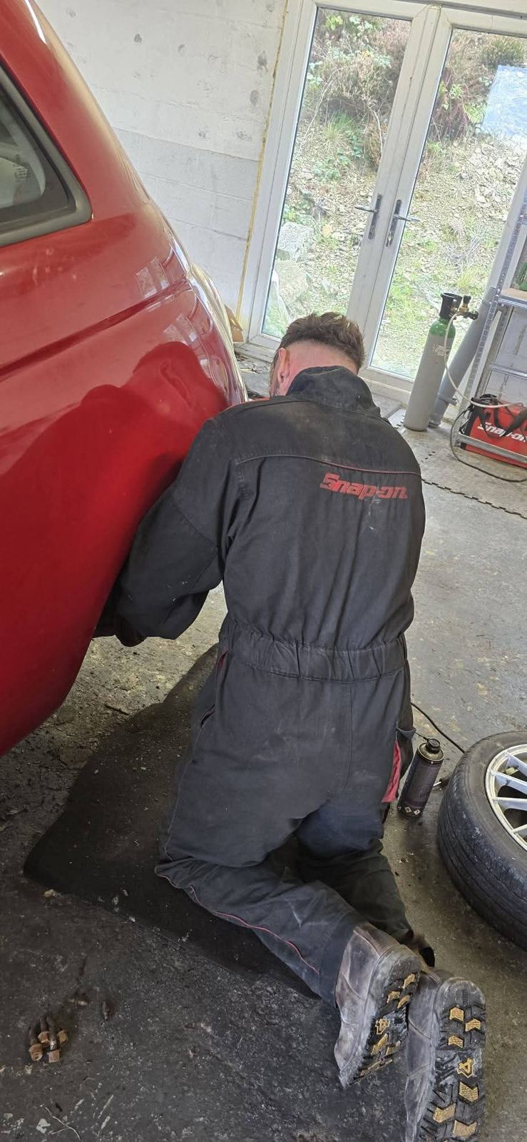 Mechanic working on the rear wheel arch of a red car